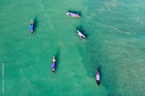 Aerial view of traditional longtail boats floating on a turquoise and clear ocean in Thailand.