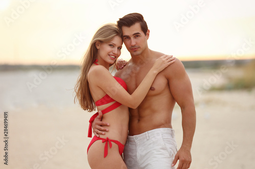 Happy young couple spending time together on sea beach at sunset