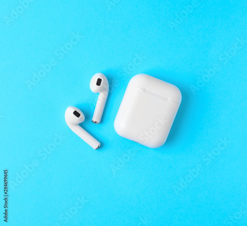 Modern wireless earphones and charging case on light blue background, flat lay. Space for text