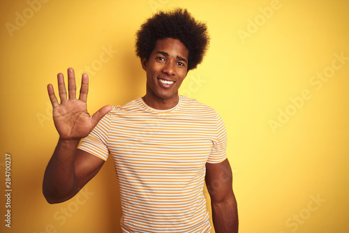 American man with afro hair wearing striped t-shirt standing over isolated yellow background showing and pointing up with fingers number five while smiling confident and happy.