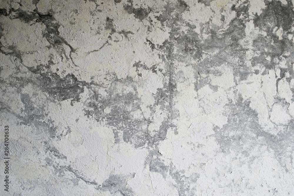 A gray concrete wall with a vertical lighting gradient interspersed with white plaster and paint. Background