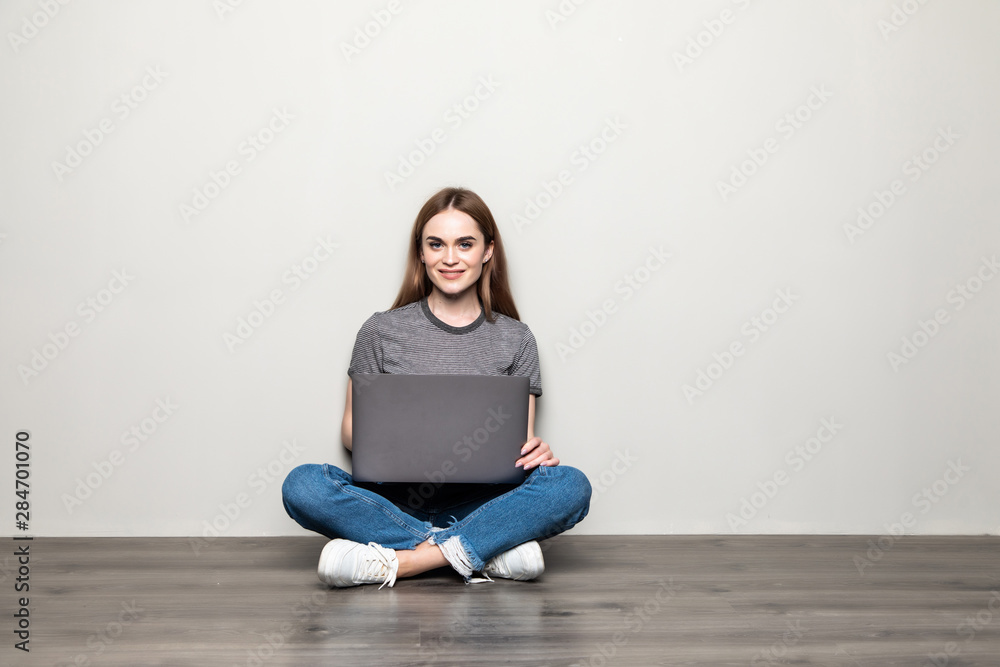 Attractive young woman holding laptop computer while sitting on the floor with legs crossed and looking away at copy space isolated over gray background Attractive young woman holding laptop computer while sitting on the floor with legs crossed and looking away at copy space isolated over gray background
