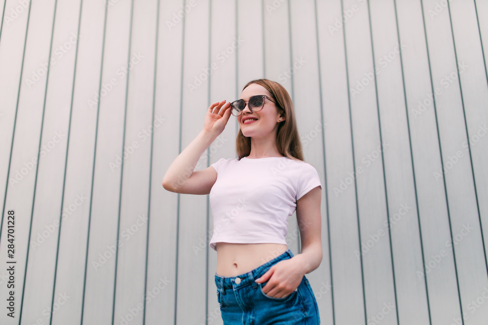 Stylish young woman white shirt posing on white striped wall background Stylish young woman white shirt posing on white striped wall background