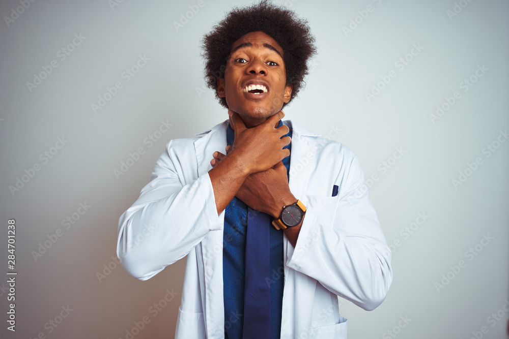 Young african american doctor man wearing coat standing over isolated white background shouting and suffocate because painful strangle. Health problem. Asphyxiate and suicide concept. Young african american doctor man wearing coat standing over isolated white background shouting and suffocate because painful strangle. Health problem. Asphyxiate and suicide concept.