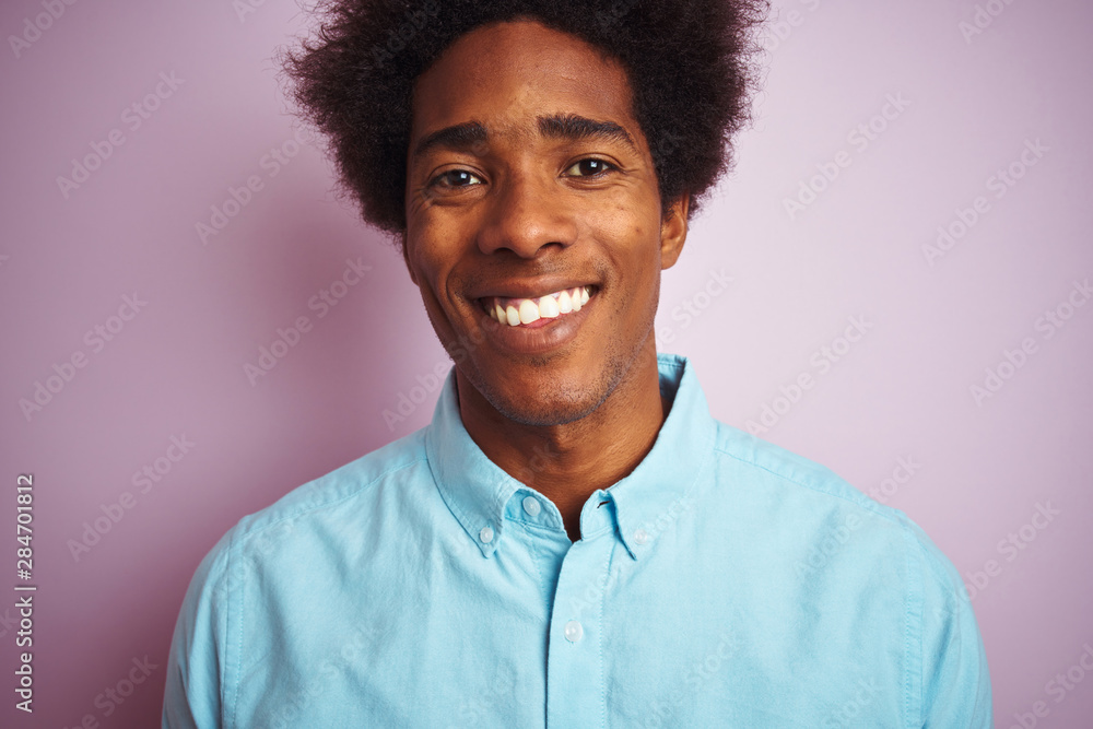 Young american man with afro hair wearing blue shirt standing over isolated pink background with a happy face standing and smiling with a confident smile showing teeth Young american man with afro hair wearing blue shirt standing over isolated pink background with a happy face standing and smiling with a confident smile showing teeth