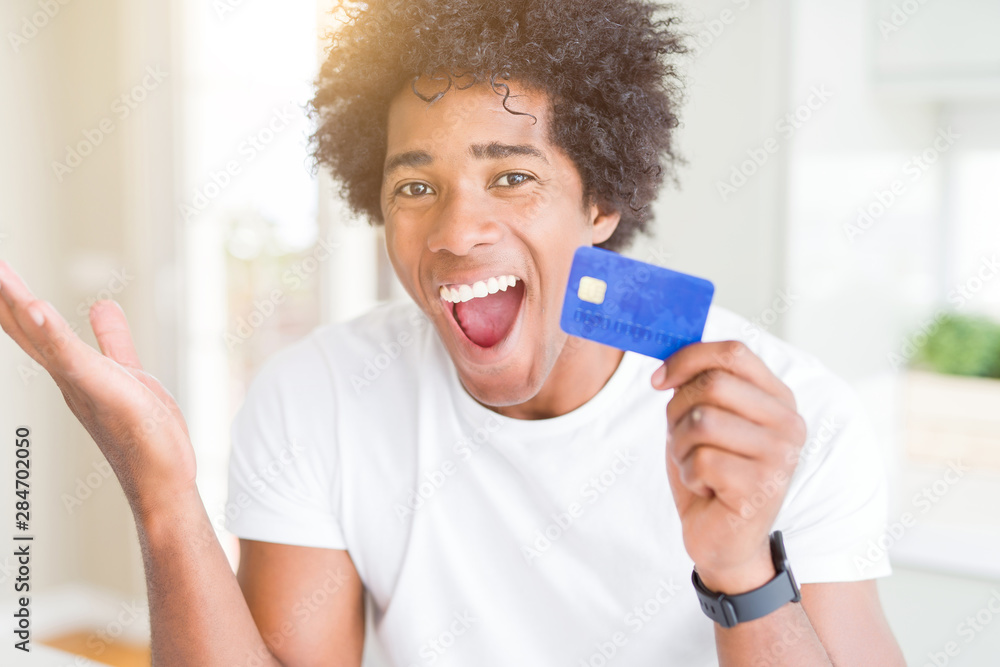 African American man holding credit card very happy and excited, winner expression celebrating victory screaming with big smile and raised hands African American man holding credit card very happy and excited, winner expression celebrating victory screaming with big smile and raised hands