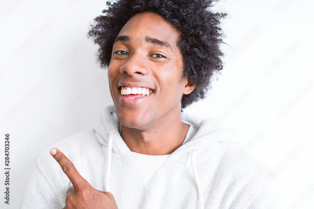 Handsome african american man with afro hair over white background cheerful with a smile of face pointing with hand and finger up to the side with happy and natural expression on face Handsome african american man with afro hair over white background cheerful with a smile of face pointing with hand and finger up to the side with happy and natural expression on face
