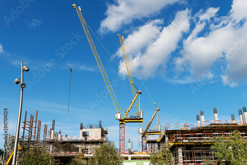 Two construction cranes on a building construction. High crane on a blue sky with clouds. The construction of a multi-storey.