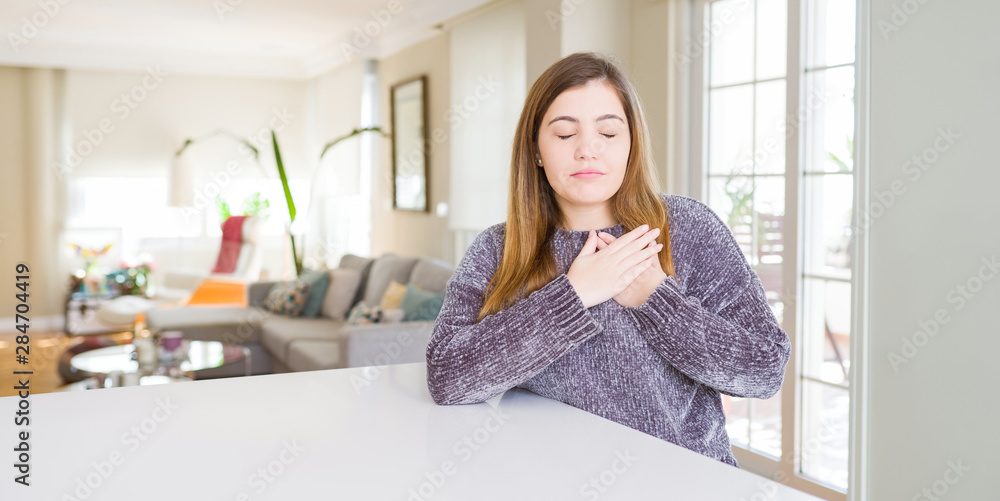Beautiful young woman at home smiling with hands on chest with closed eyes and grateful gesture on face. Health concept.
