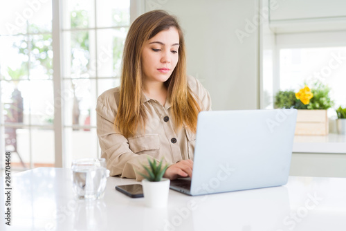 Beautiful young woman using computer laptop with a confident expression on smart face thinking serious