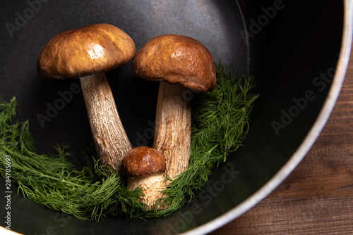 wooden tray with porcini mushrooms and mushrooms in a black pan on a wooden table. Ingredients before cooking. Mushrooms in a black pan