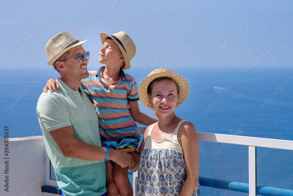 Family of three people on hotel balcony against sea in summer enjoying their vacation. Fathers is holding son on hands.