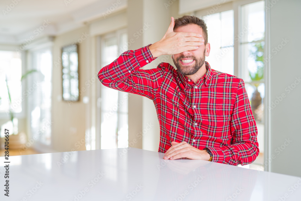 Handsome man wearing colorful shirt smiling and laughing with hand on face covering eyes for surprise. Blind concept. Handsome man wearing colorful shirt smiling and laughing with hand on face covering eyes for surprise. Blind concept.