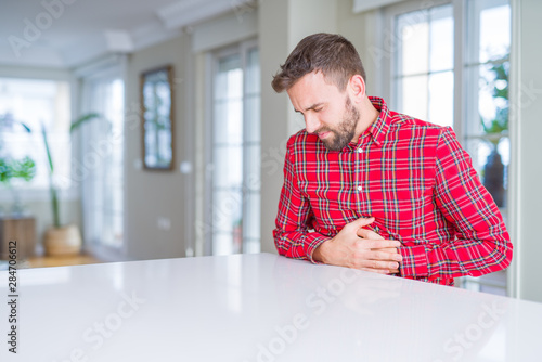 Handsome man wearing colorful shirt with hand on stomach because nausea, painful disease feeling unwell. Ache concept. © Krakenimages.com