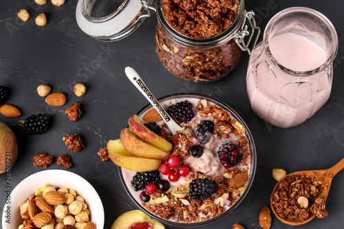 Granola crispy honey muesli with natural yogurt, fresh berries and fruit, chocolate and nuts in a glass bowl against a dark background, horizontal orientation, top view photo