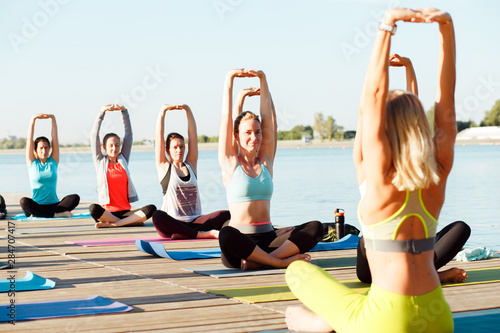 A big group of people attending yoga classes on a pontoon near the lake.