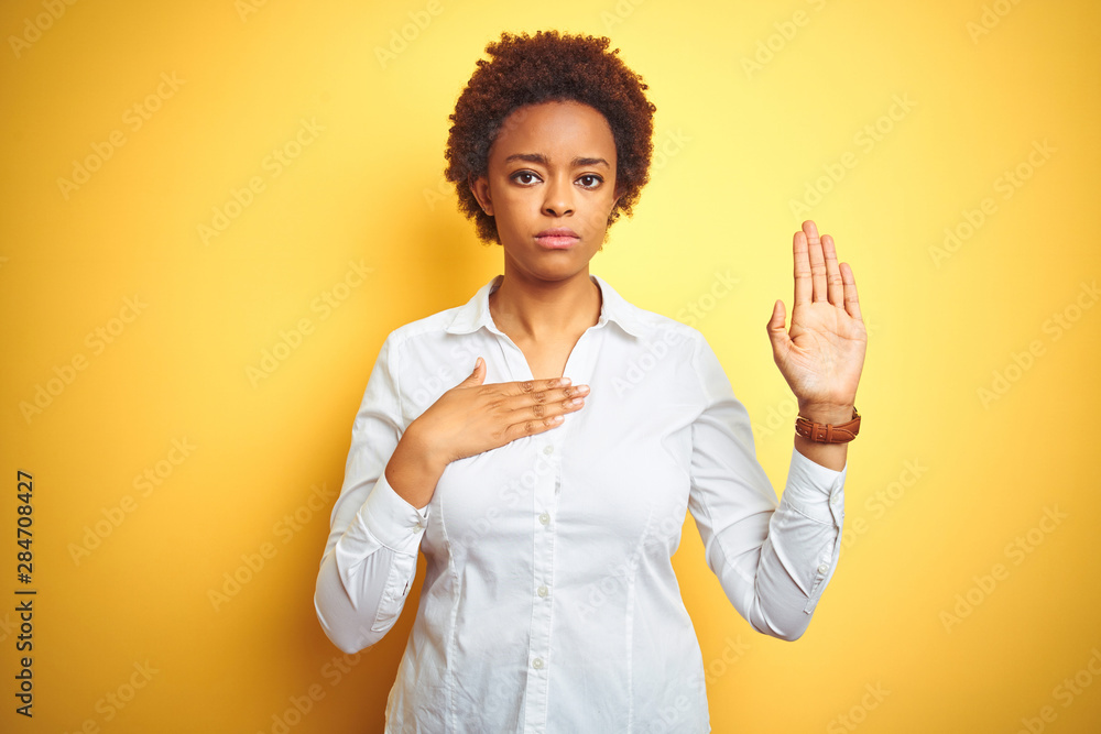 African american business woman over isolated yellow background Swearing with hand on chest and open palm, making a loyalty promise oath African american business woman over isolated yellow background Swearing with hand on chest and open palm, making a loyalty promise oath