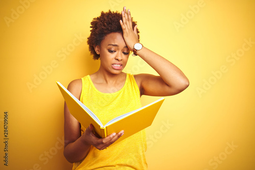African american woman reading a book over yellow isolated background stressed with hand on head, shocked with shame and surprise face, angry and frustrated. Fear and upset for mistake.