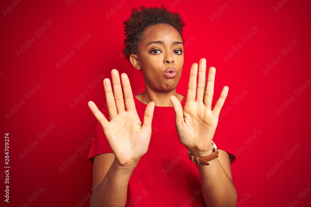 Young beautiful african american woman with afro hair over isolated red background Moving away hands palms showing refusal and denial with afraid and disgusting expression. Stop and forbidden. Young beautiful african american woman with afro hair over isolated red background Moving away hands palms showing refusal and denial with afraid and disgusting expression. Stop and forbidden.