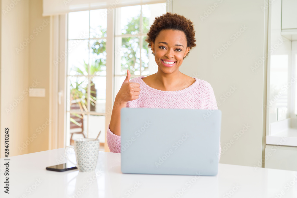 Young african american woman working using computer laptop doing happy thumbs up gesture with hand. Approving expression looking at the camera with showing success. Young african american woman working using computer laptop doing happy thumbs up gesture with hand. Approving expression looking at the camera with showing success.