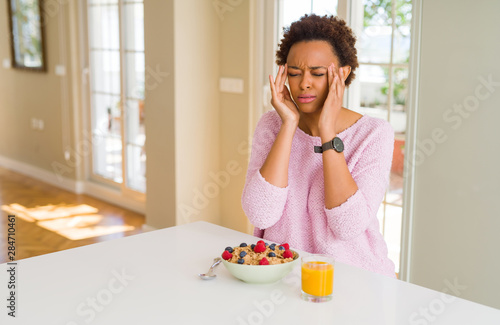 Young african american woman having healthy breakfast in the morning at home with hand on head for pain in head because stress. Suffering migraine.
