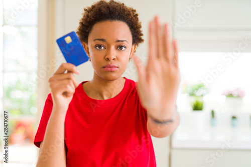 Young african american woman holding credit card with open hand doing stop sign with serious and confident expression  defense gesture