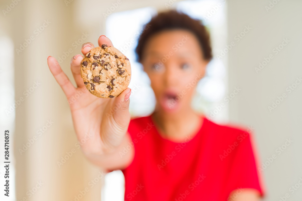 Young african american woman eating chocolate chips cookies scared in shock with a surprise face, afraid and excited with fear expression Young african american woman eating chocolate chips cookies scared in shock with a surprise face, afraid and excited with fear expression