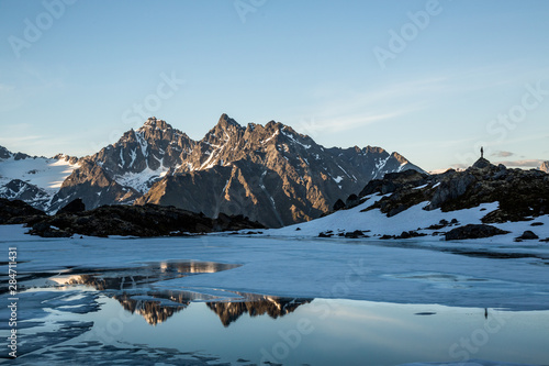 Spring thaw on remote alpine lake in the Talkeetna Mountains of Alaska. Man standing on ridge reflected in the lake. photo