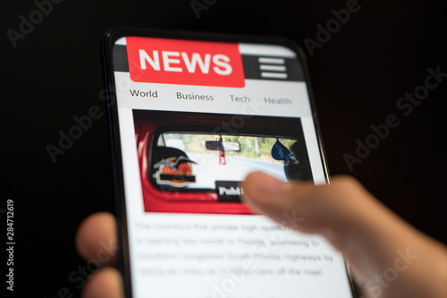 A man holding mobile smart phone with news on screen. Newspaper online portal in browser.