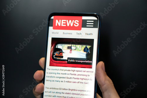 A man holding mobile smart phone with news on screen. Newspaper online portal in browser.