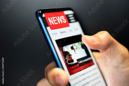 A man holding mobile smart phone with news on screen. Newspaper online portal in browser.