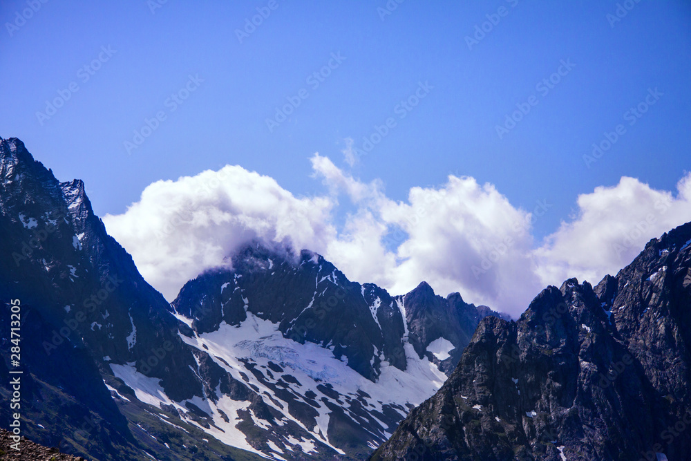 Horizontal beautiful panorama of the Caucasus mountains. The top of the mountain range covered with snow. Forest on the slope. Sunny day. Background image for travel and nature.