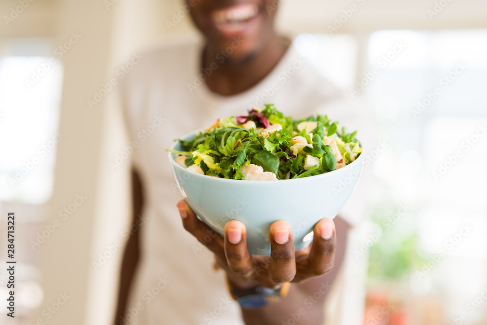 African young man holding a bowl of healthy salad smiling cheerful