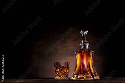 Glass of whiskey with ice and decanter on dark wood background photo