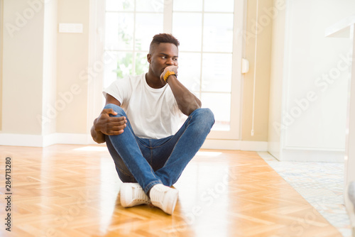 Handsome african american man sitting on the floor at home thinking looking tired and bored with depression problems with crossed arms. © Krakenimages.com