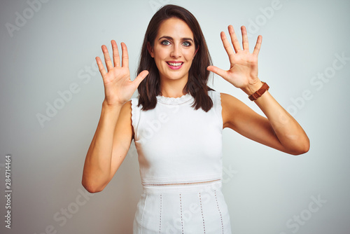 Young beautiful woman wearing dress standing over white isolated background showing and pointing up with fingers number ten while smiling confident and happy.