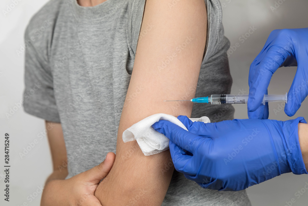 The process of administering the vaccination to the upper shoulder of a school-age boy. Doctor's hands in gloves, holding syringe with incision The process of administering the vaccination to the upper shoulder of a school-age boy. Doctor's hands in gloves, holding syringe with incision