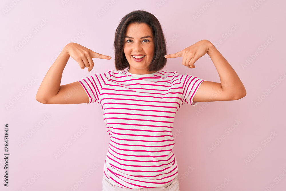 Young beautiful woman wearing striped t-shirt standing over isolated pink background smiling cheerful showing and pointing with fingers teeth and mouth. Dental health concept. Young beautiful woman wearing striped t-shirt standing over isolated pink background smiling cheerful showing and pointing with fingers teeth and mouth. Dental health concept.