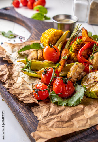 Vegan Grill menu, Grilled vegetables - zucchini, paprika, сherry tomatoes, corn, carrots and champignons served on wooden board at white background, vertical orientation