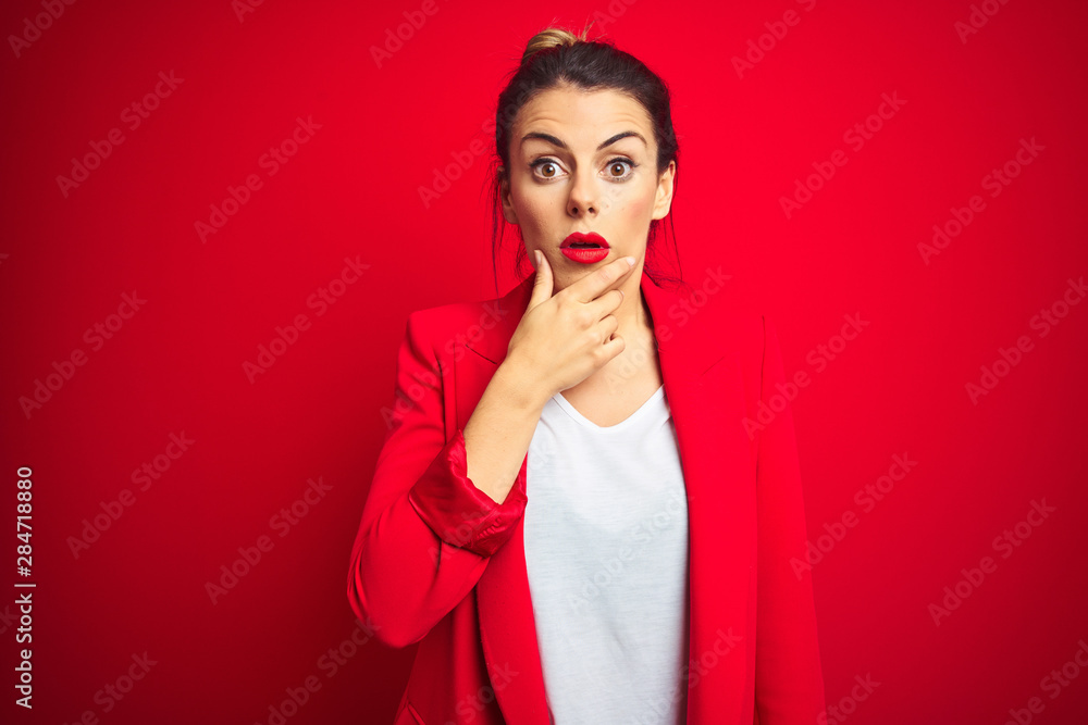 Young beautiful business woman standing over red isolated background Looking fascinated with disbelief, surprise and amazed expression with hands on chin Young beautiful business woman standing over red isolated background Looking fascinated with disbelief, surprise and amazed expression with hands on chin