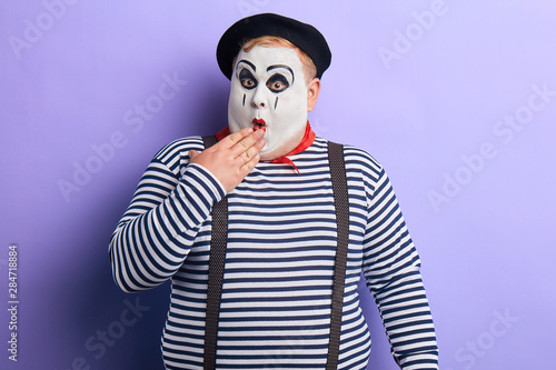 Fényképezés Shocked funny mime artist standing in disbelief closing his mouth with a palm isolated on blue background