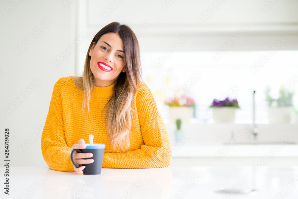 Young beautiful woman drinking a cup of coffee at home with a happy face standing and smiling with a confident smile showing teeth Young beautiful woman drinking a cup of coffee at home with a happy face standing and smiling with a confident smile showing teeth