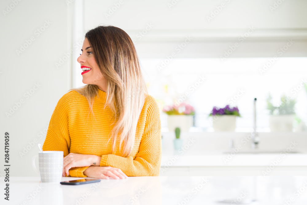 Young beautiful woman drinking a cup of coffee at home looking away to side with smile on face, natural expression. Laughing confident. Young beautiful woman drinking a cup of coffee at home looking away to side with smile on face, natural expression. Laughing confident.
