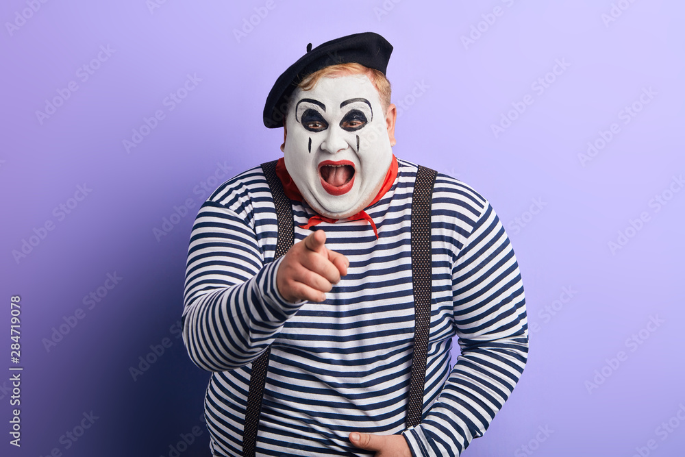 laughing crazy plump mime with wide open mouth points with finger at you, happiness, emotion and feeling. close up portrait, isolated blue background, studio shot laughing crazy plump mime with wide open mouth points with finger at you, happiness, emotion and feeling. close up portrait, isolated blue background, studio shot