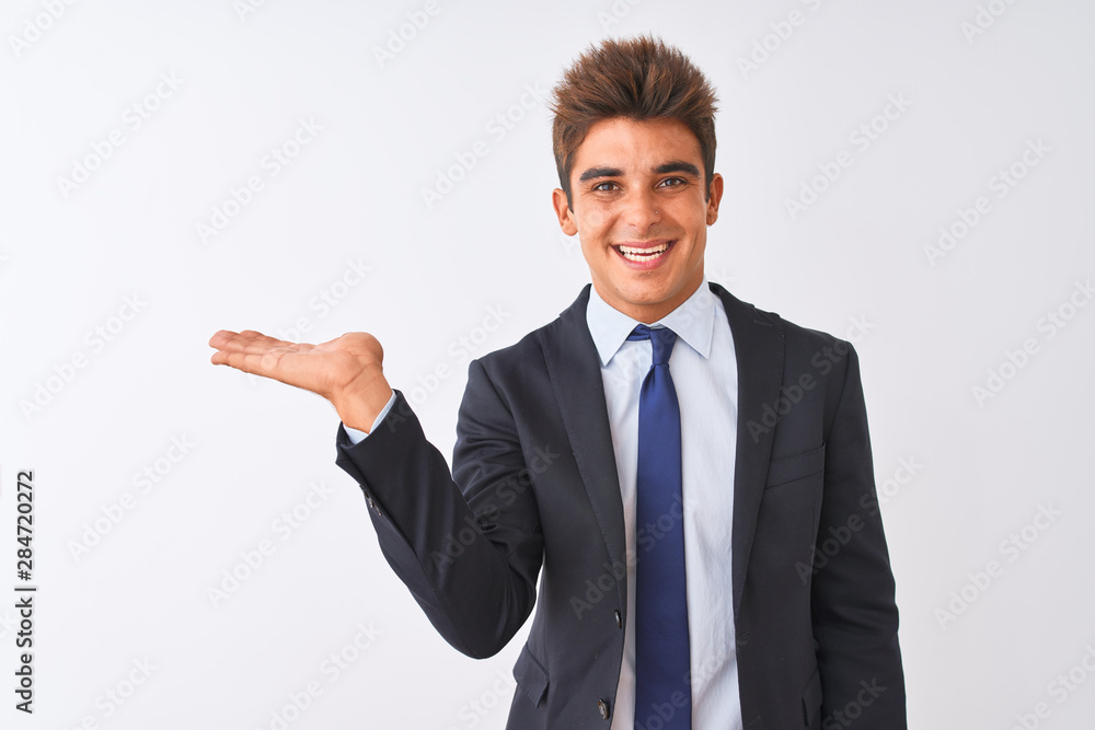 Young handsome businessman wearing suit standing over isolated white background smiling cheerful presenting and pointing with palm of hand looking at the camera. Young handsome businessman wearing suit standing over isolated white background smiling cheerful presenting and pointing with palm of hand looking at the camera.