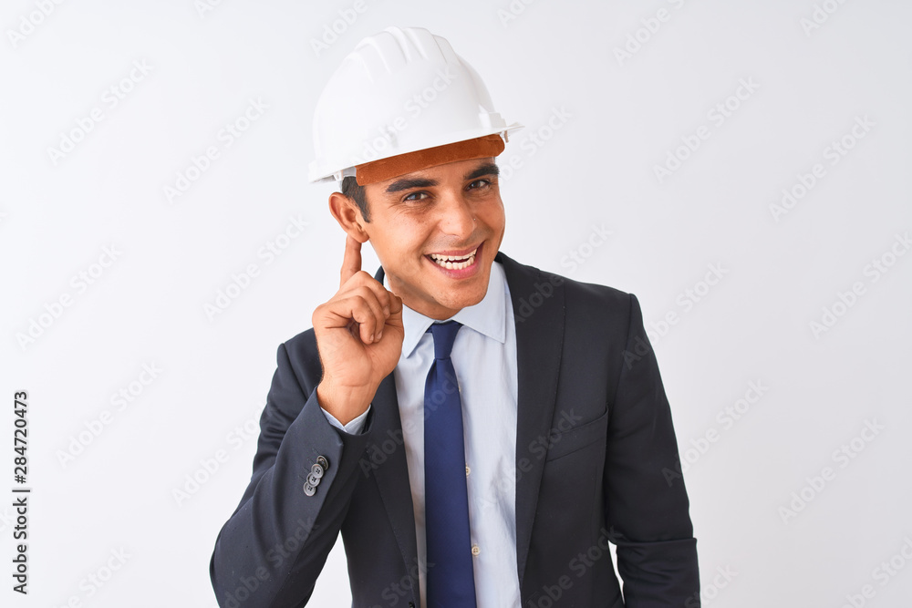 Young handsome architect man wearing suit and helmet over isolated white background smiling with hand over ear listening an hearing to rumor or gossip. Deafness concept. Young handsome architect man wearing suit and helmet over isolated white background smiling with hand over ear listening an hearing to rumor or gossip. Deafness concept.