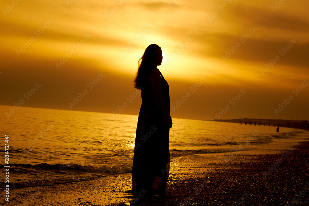 Silhouette of a girl in golden sunset by the sea