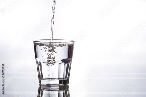 Pure drinking water in a glass cup. A stream of water and transparent droplets on the wall of the glass.