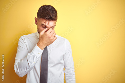 Young handsome business man wearing elegant white shirt over yellow isolated background tired rubbing nose and eyes feeling fatigue and headache. Stress and frustration concept.