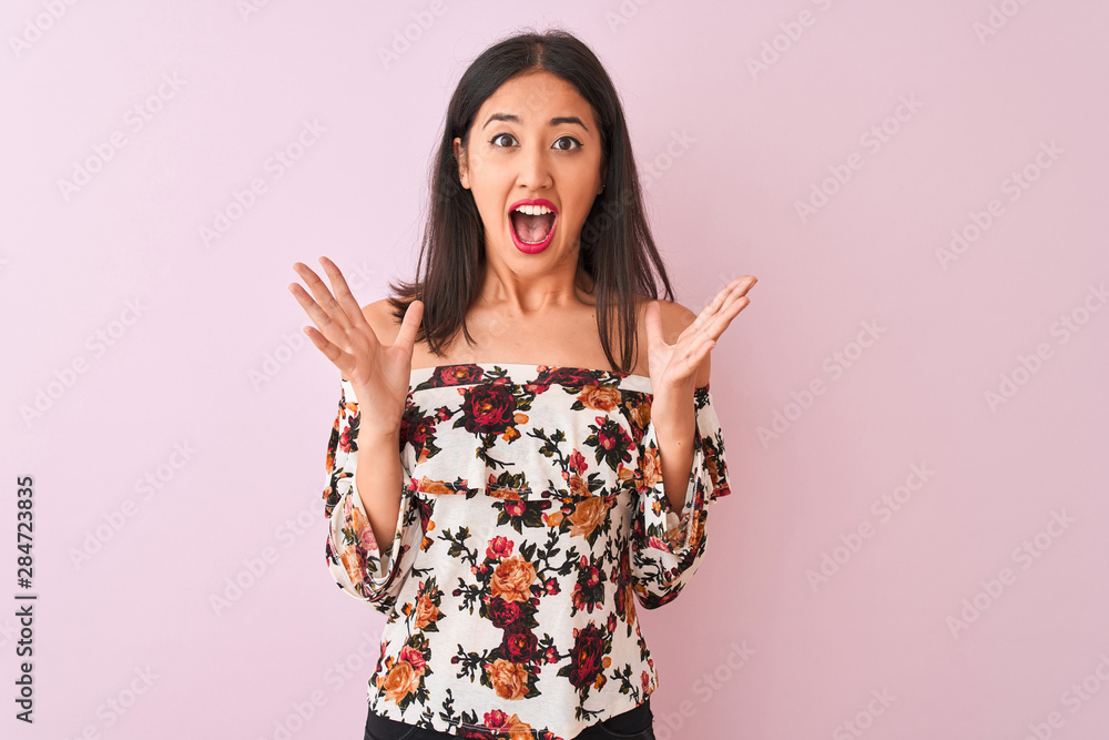 Young chinese woman wearing floral t-shirt standing over isolated pink background celebrating crazy and amazed for success with arms raised and open eyes screaming excited. Winner concept Young chinese woman wearing floral t-shirt standing over isolated pink background celebrating crazy and amazed for success with arms raised and open eyes screaming excited. Winner concept